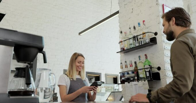 Handsome bearded man paying for takeaway coffee with mobile phone at coffee shop. Worker serving a customer who uses smartphone to pay in coffee shop.