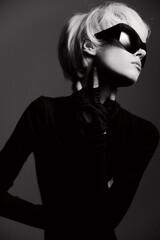 Stylish woman with short hair wearing oversized sunglasses, striking a bold pose against a dark backdrop. Fashion and confidence concept.