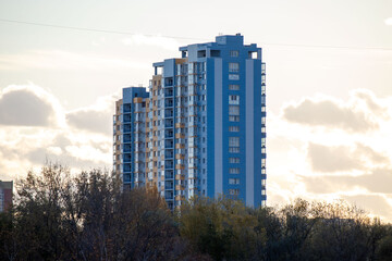 A tall building with a blue facade is seen against a cloudy sky