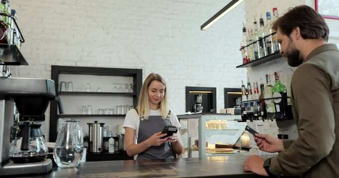In the cafe woman makes takeaway coffee for a customer who pay using credit card contactless payment spending money in cafe with digital transaction service.