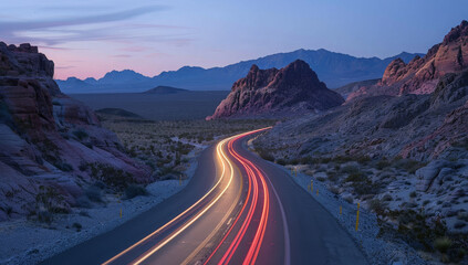 A winding road through rocky terrain at dusk, showcasing light trails from passing vehicles.