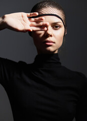 Thoughtful young woman with netted headband, posing against a dark background, expressing deep contemplation and strength through her gaze and posture.