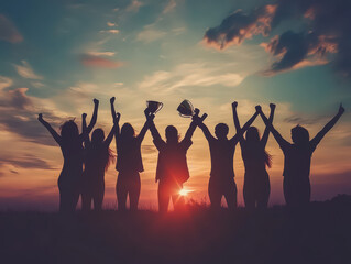 Silhouetted group celebrating success with trophies against a vibrant sunset sky.