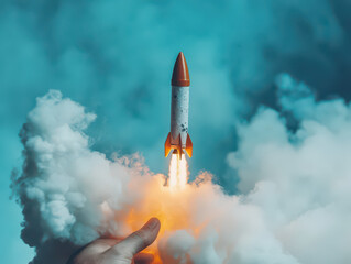 A hand guiding a miniature rocket launching amidst a cloud of smoke against a vibrant blue sky.