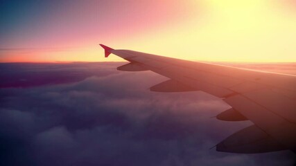 Witness a stunning sunset from an airplane window above the clouds, capturing vibrant colors and serene skies during evening travel in the sky