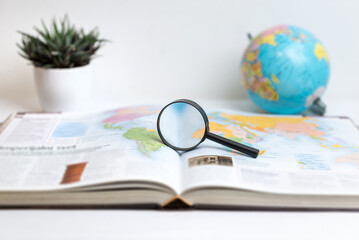 Magnifying glass on open book displaying world map with globe in background. Ideal for themes of global research, travel, geography, exploration, and education visuals © Stanisic Vladimir
