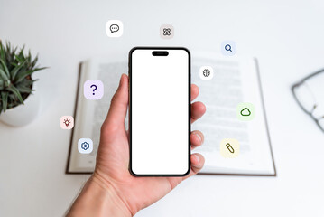 Phone mockup in hand in front of open book with flying icons: question mark, idea, cloud, pen,...