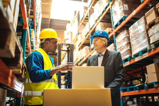 Warehouse worker discussing logistics with manager over a laptop