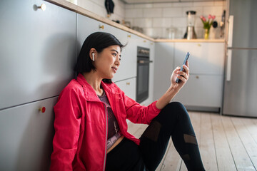 Asian woman using smartphone in kitchen after home workout