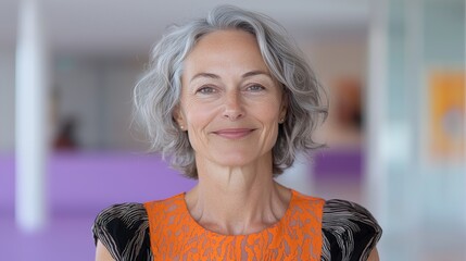 Fototapeta premium Confident mature woman with gray hair smiling in colorful dress against modern background in bright environment