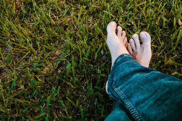 View of crossed legs in jeans with bare male feet resting on grass, with copy space