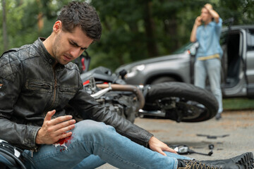 Motorcyclist sits on the asphalt near motorcycle, after road accidents with car. Broken and wrecked motorcycle on road