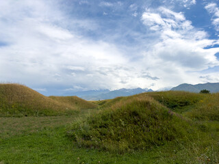 Green hilly landscape with scenic mountains in the background under a clear blue sky in the foothills of Kyrgyzstan.