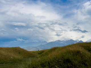 Fototapeta premium Green hilly landscape with scenic mountains in the background under a clear blue sky in the foothills of Kyrgyzstan.