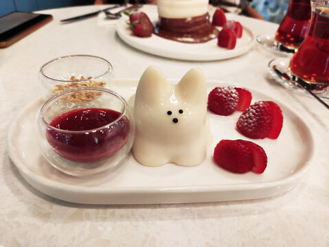 Delicious sweet white Japanese dessert, pudding in the shape of a cat, on a plate with strawberries and fruit sauce