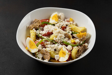 Fresh salad with tomatoes, eggs, feta cheese and paprika on black background.