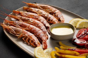 Grilled shrimps with lemon, paprika and sauce on dark background.