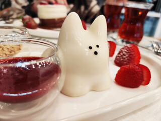 Delicious sweet white Japanese dessert, pudding in the shape of a cat, on a plate with strawberries and fruit sauce