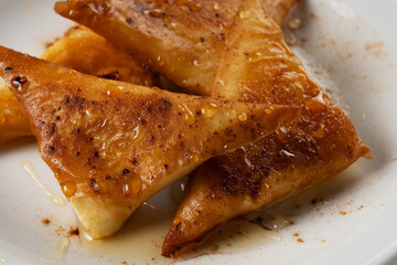 Mini cheese pies with myzithra, cretan honey and cinnamon on white plate.