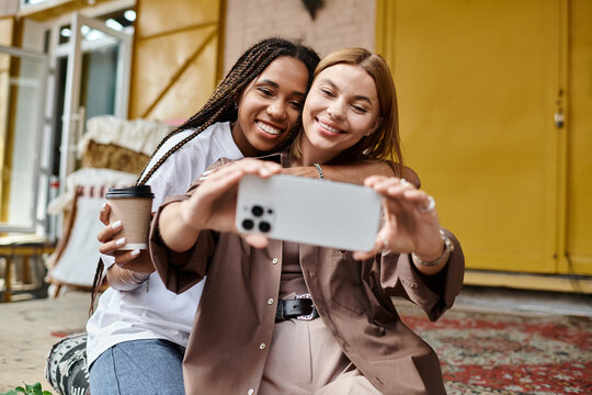 A joyful multiethnic couple shares laughter and coffee while taking a selfie in a cozy cafe setting. - Powered by Adobe