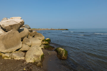 Large rocks on the shore of the Caspian Sea. In the background, fishermen stand on the shore and fish with a rod.