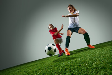 Competitive and motivated young women, soccer players in dynamic motion, competing on field over control of ball. Under rainy weather. Concept of sport, action, competition, game, tournament