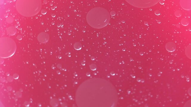 Una toma de cerca de varias burbujas de agua y aceite en movimiento en un fondo de color rosado