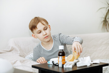 Sick little kid teen boy sits on bed at home and take medication. Flu season. Healthcare concept.