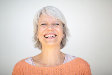 Smiling woman in orange sweater with short gray hair on white background