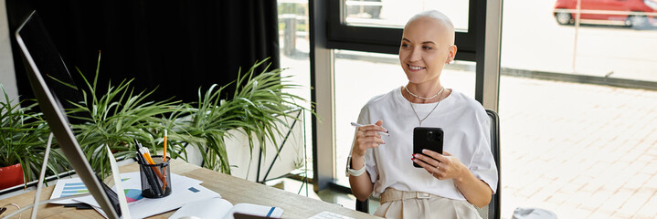The young bald woman radiates happiness as she engages with her smartphone at a modern workspace.