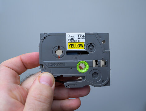 Frankfurt, Germany - Dec 24, 2023: Hand holding a Brother TZ label tape cartridge, 9mm width, flexible ID, with yellow labeling tape - Ideal for labeling and organizing