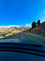 Obraz premium View of snow-capped peaks and mountain slopes from a car window during an autumn journey in Kyrgyzstan.