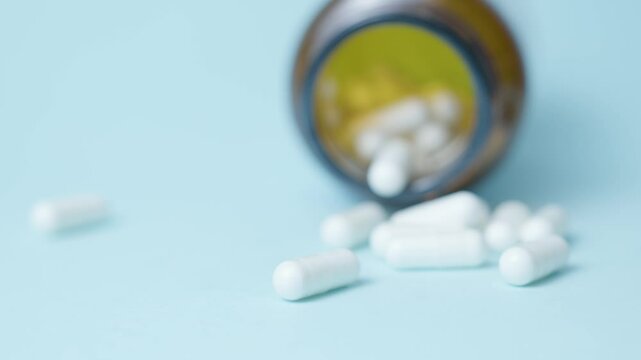 A jar with white capsules medication or supplements isolated on light blue background. Racking focus. High quality 4k footage