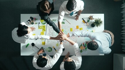 Top down view of business team discussing about using clean energy and sustainable investment at meeting table with wind mill, document with environmental graph and wooden house model. Alimentation.