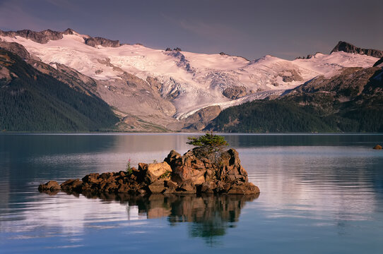 Tranquil lake and mountains with snow, and a small landform in the middle of the lake