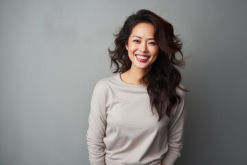 Obraz premium Portrait of a satisfied asian woman in her 30s showing off a thermal merino wool top over blank studio backdrop
