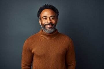 Obraz premium Portrait of a content afro-american man in his 40s dressed in a warm wool sweater while standing against blank studio backdrop