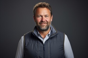 Fototapeta premium Portrait of a cheerful man in his 40s dressed in a water-resistant gilet isolated in blank studio backdrop