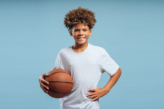 Portrait of smiling, happy African American boy, teenager holding basketball looking at camera