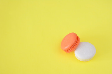 two orange and white macaronis are on a yellow table copy space