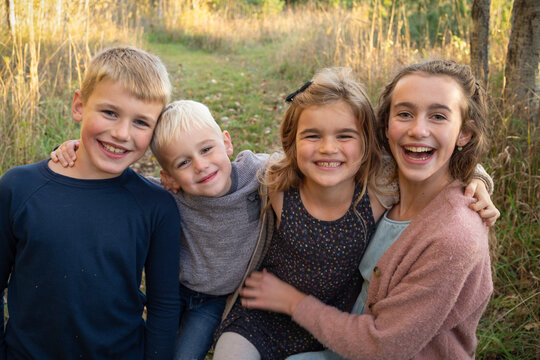 Close-up portrait of four siblings with arms around each other smiling at the camera in a rural setting in Beckwith Township at Carleton Place in the Ottawa Valley; Ontario, Canada