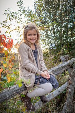 Close-up portrait of a young girl sitting on a wooden fence, smiling at the camera in a rural setting in the Fall, Beckwith Township at Carleton Place in the Ottawa Valley; Ontario, Canada