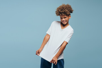 Cheerful, attractive African American boy with curly hairstyle wearing white t shirt with mockup