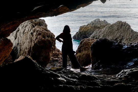 Woman stands on the rocks at low tide in the Cave of Lapa de Santa Margarida; Sao Lourenco, Setubal, Portugal