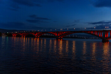 Illuminated bridge over river at dusk with reflections on wate