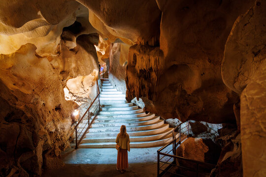 Rear view of a woman standing on a path at the bottom of steps in an illuminated marine cave, Treasure Cave, in Malaga, Spain; Rincon de la Victoria, Costa del Sol, Malaga Province, Spain