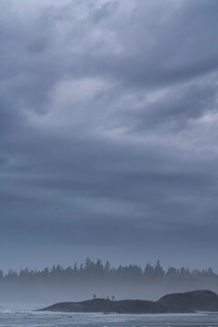 People exploring the rocks that are along Long Beach, just outside of Tofino on Vancouver Island.  Moody conditions exist as a storm quickly approaches; Tofino, British Columbia, Canada