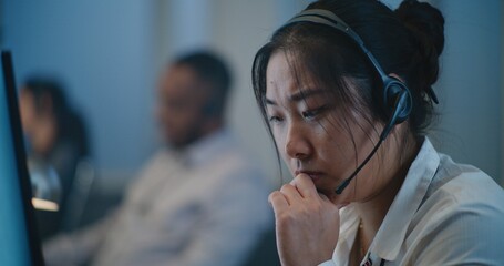 Call center office of emotional support line: Portrait of stressed Asian female hotline operator in headset consulting person on call, providing psychological help. Online mental health professional.