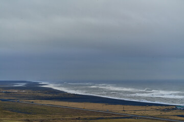 Ocean waves crashing on black sand beach under cloudy sky