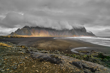 Dramatic sky covering mountain range with black sand beach in foreground